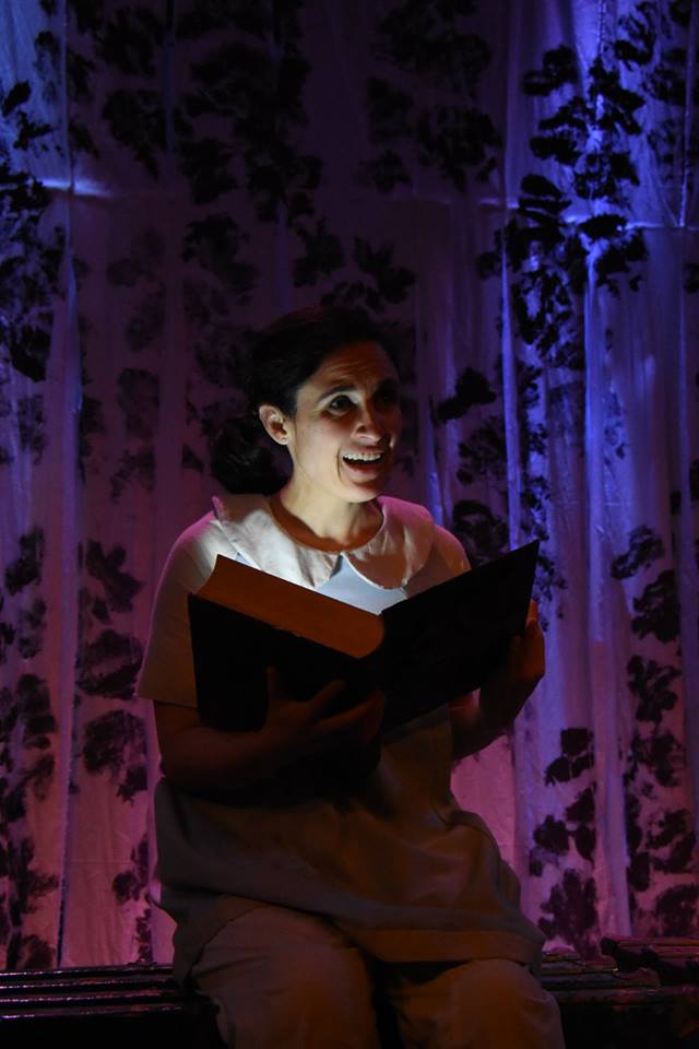 Photo of María Leigh (Iro) holding open a glowing book. From Custom Made Theatre Company's world premiere Of Serpants & Sea Spray production, 2016. Photo by Jay Yamada.